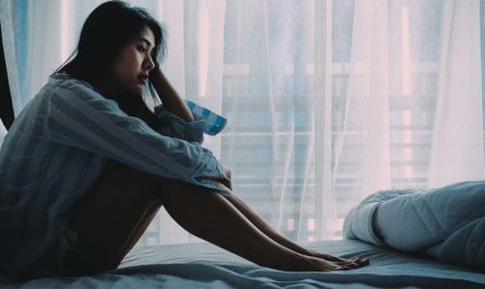 Asian woman sitting on a bed looking sad
